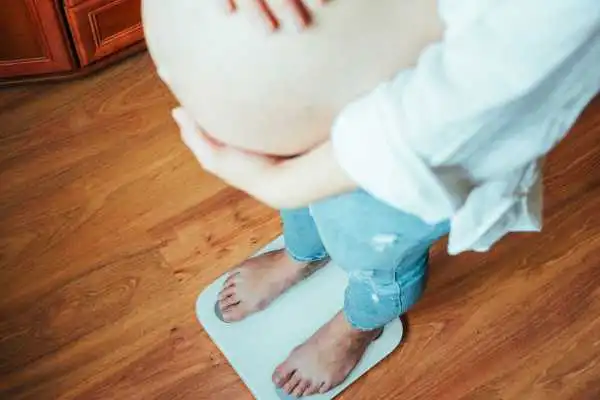Image of woman weighing herself and experiencing weight gain through pregnancy Great Missenden
